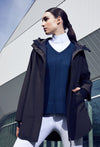 Woman wearing white riding leggings, blue knit sweater, white turtle neck riding shirt and brown overcoat.