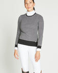 Woman wearing white riding leggings with a great, knit sweater that features black elbow patches and a black trim.
