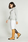 Woman wearing white knit sweater and white riding pants.