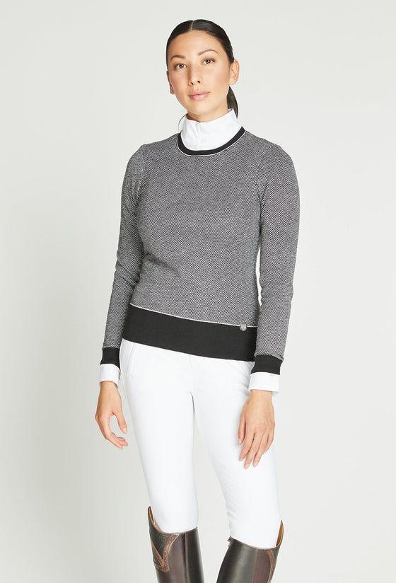 Woman wearing white riding leggings with a great, knit sweater that features black elbow patches and a black trim.
