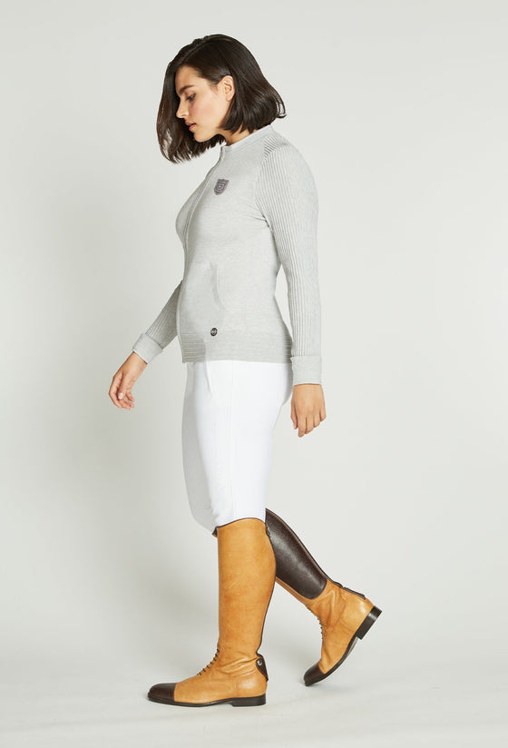 Woman wearing white knit sweater and white riding pants.