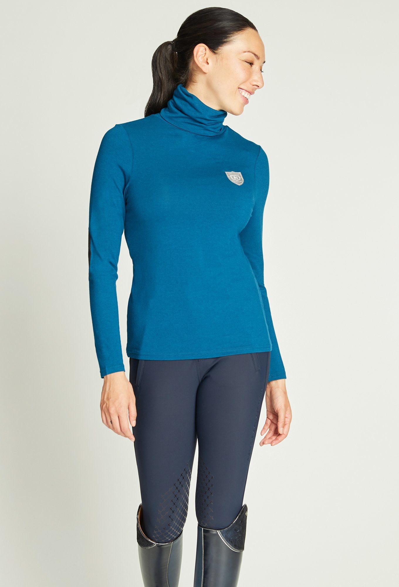 Woman wearing blue riding top and navy riding leggings.