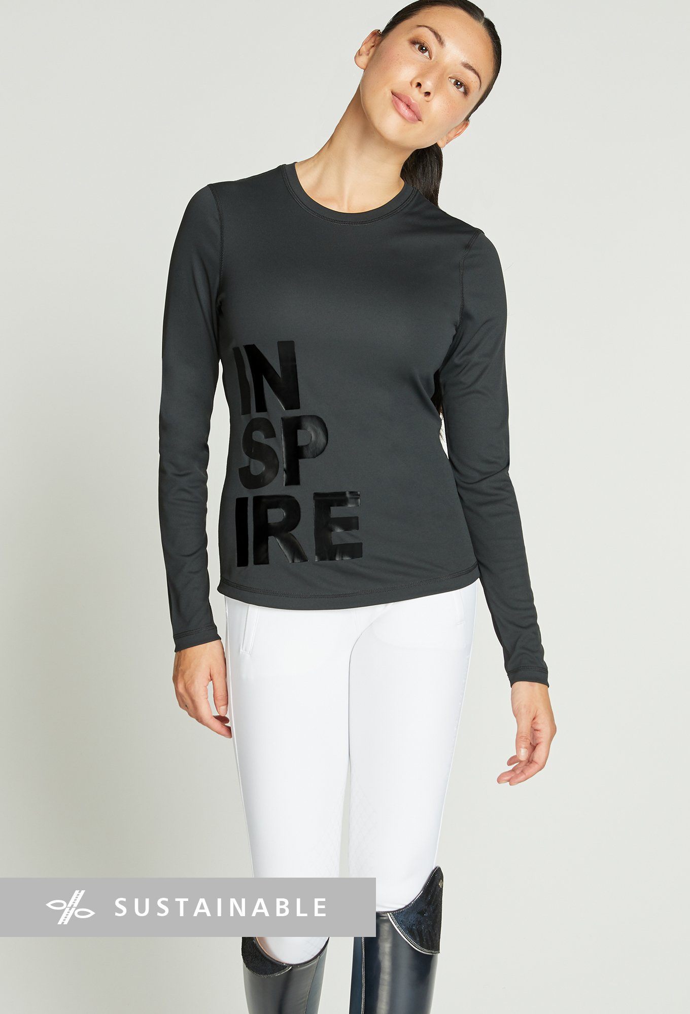Woman wearing long-sleeve black riding top with lettering reading &quot;Inspire&quot; on the right of the top.