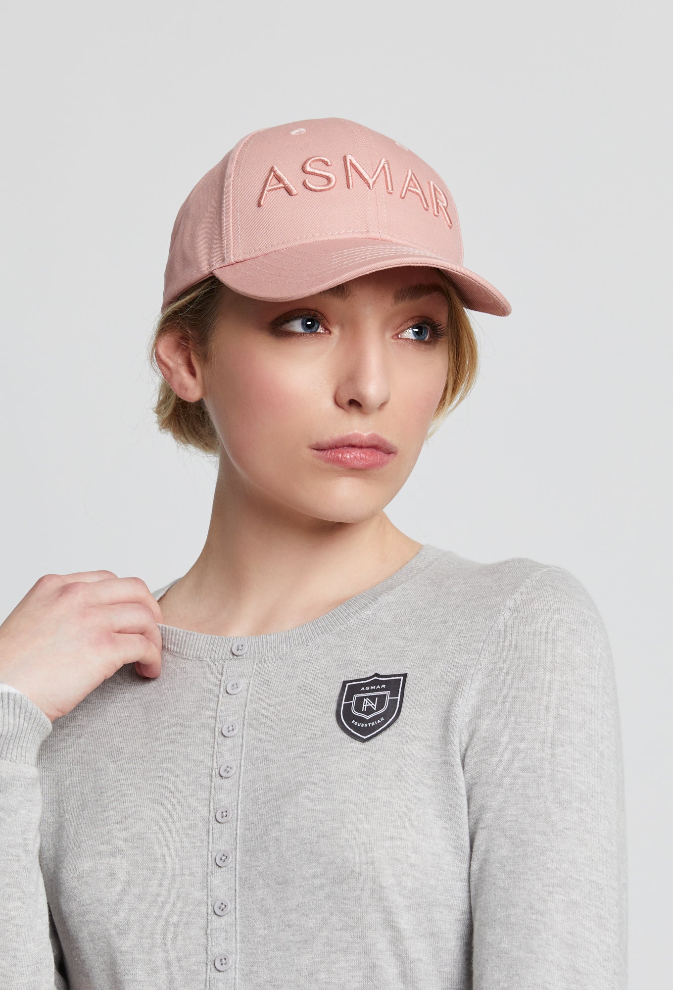 Woman wearing a pink baseball style cap with the word &quot;Asmar&quot; written on the front.